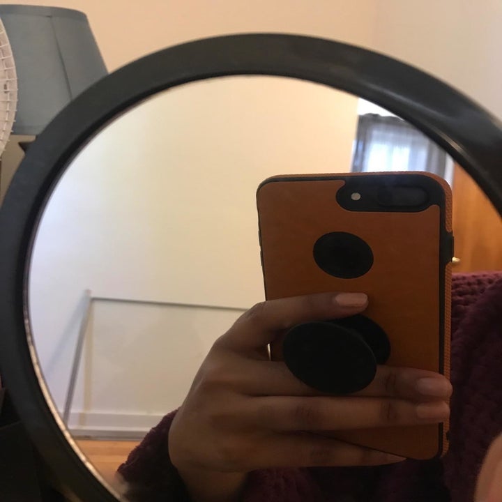 reviewer holding the phone grip between their fingers taking a picture in a mirror to show how the grip works
