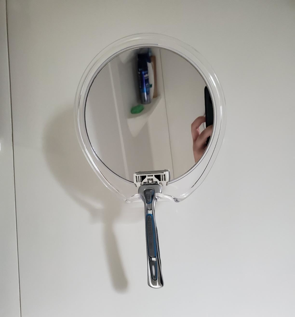 reviewer image of the mirror on a shower wall with a razor hanging off the build in razor holder