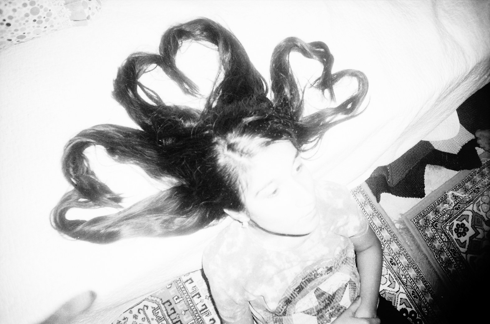 A girl sits on the edge of the bed with her long hair arranged to form hearts