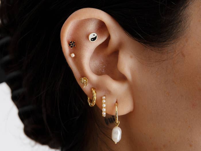 a model wearing a mix of gold earrings and earrings with pearl details