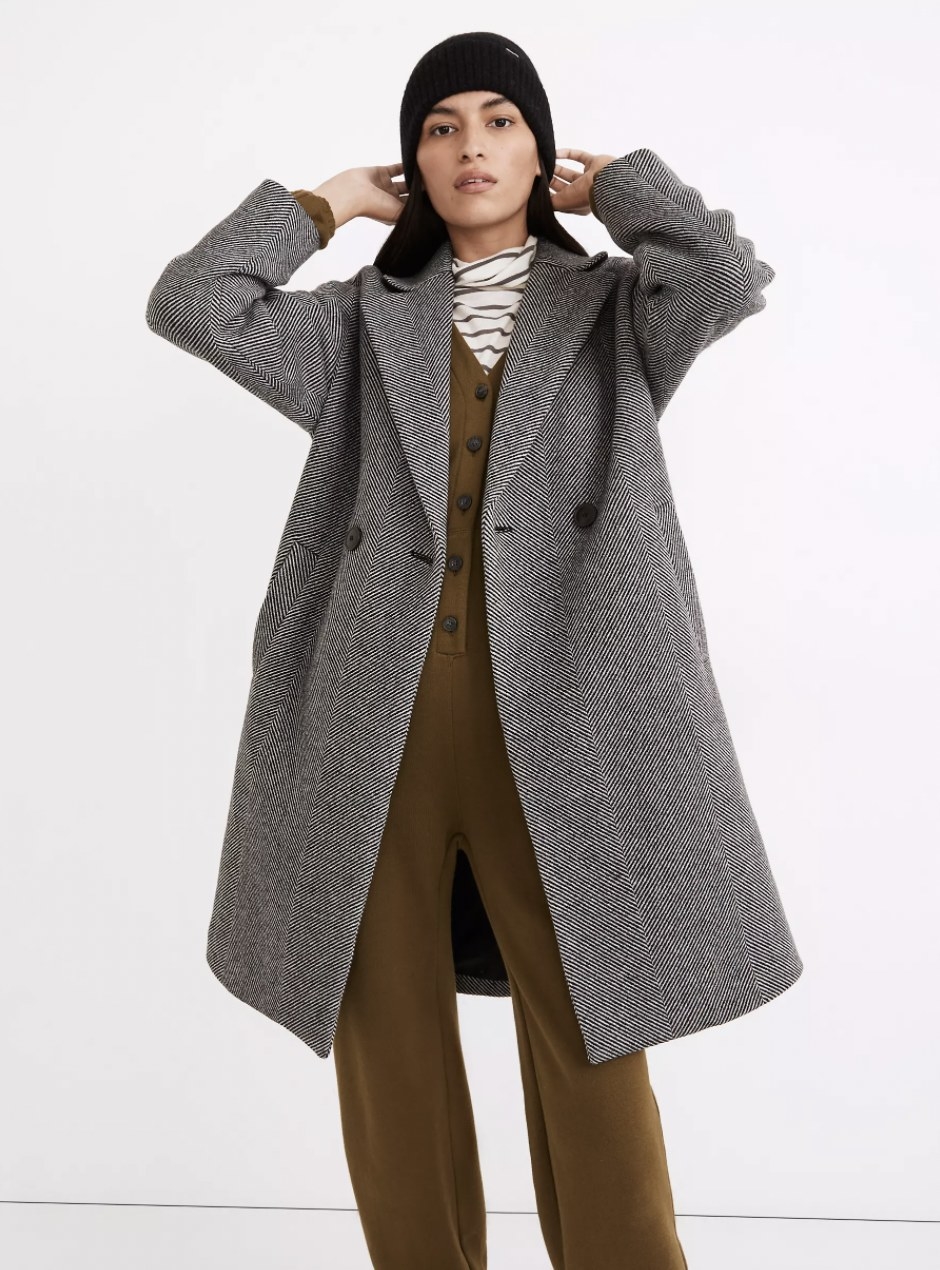 a model wearing the coat in a black and white herringbone design. the jacket hits right above the knee