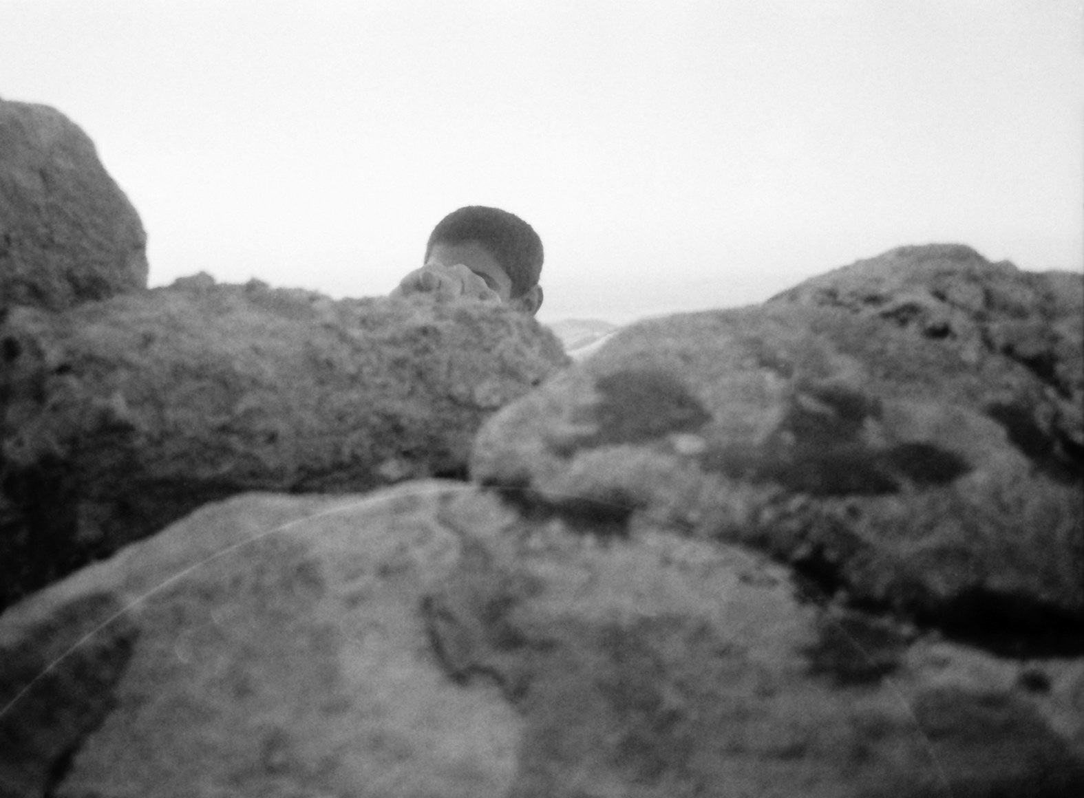 A boy&#x27;s head is barely visible over a grouping of rocks 