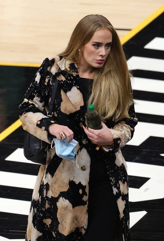 Adele walking at an NBA basketball game and holding a water bottle and a face mask