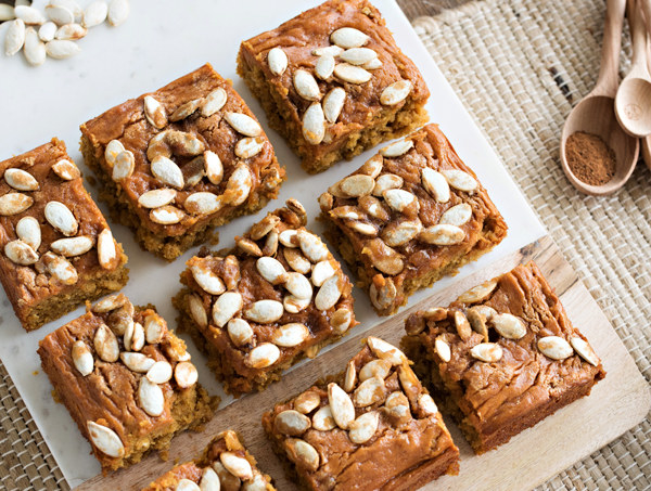 cutting board with pumpkin cream cheese bars topped with pumpkin seeds