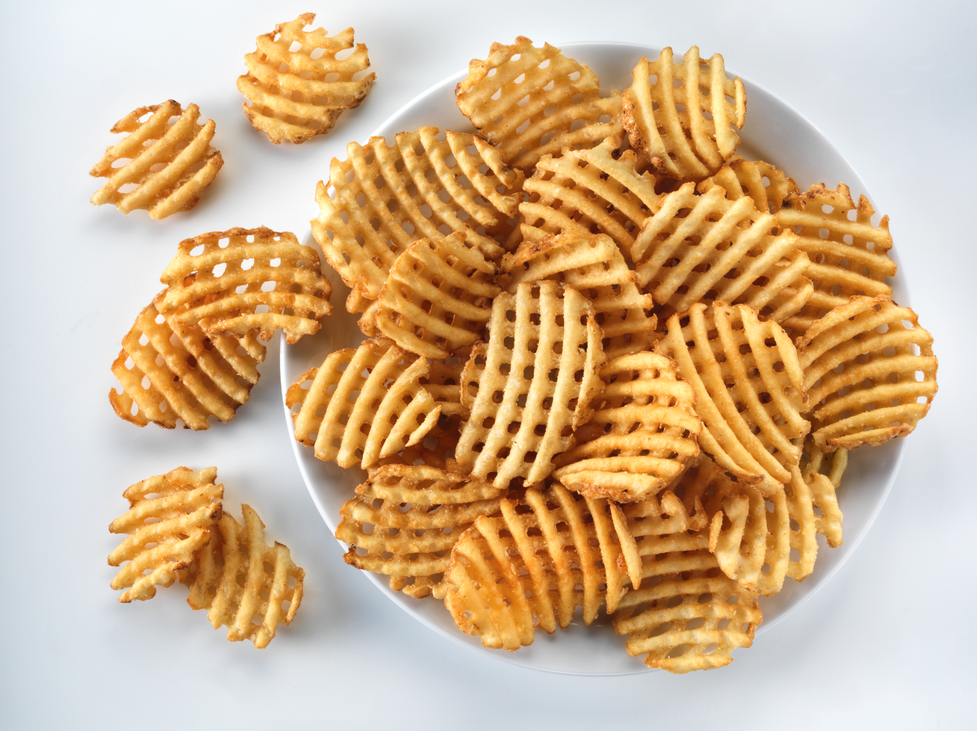 A plate of waffle fries on a white surface.