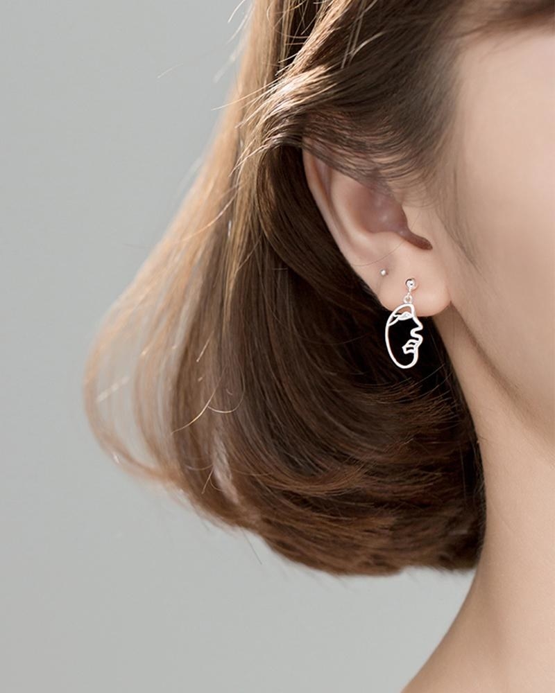A person wearing earrings that look like small faces