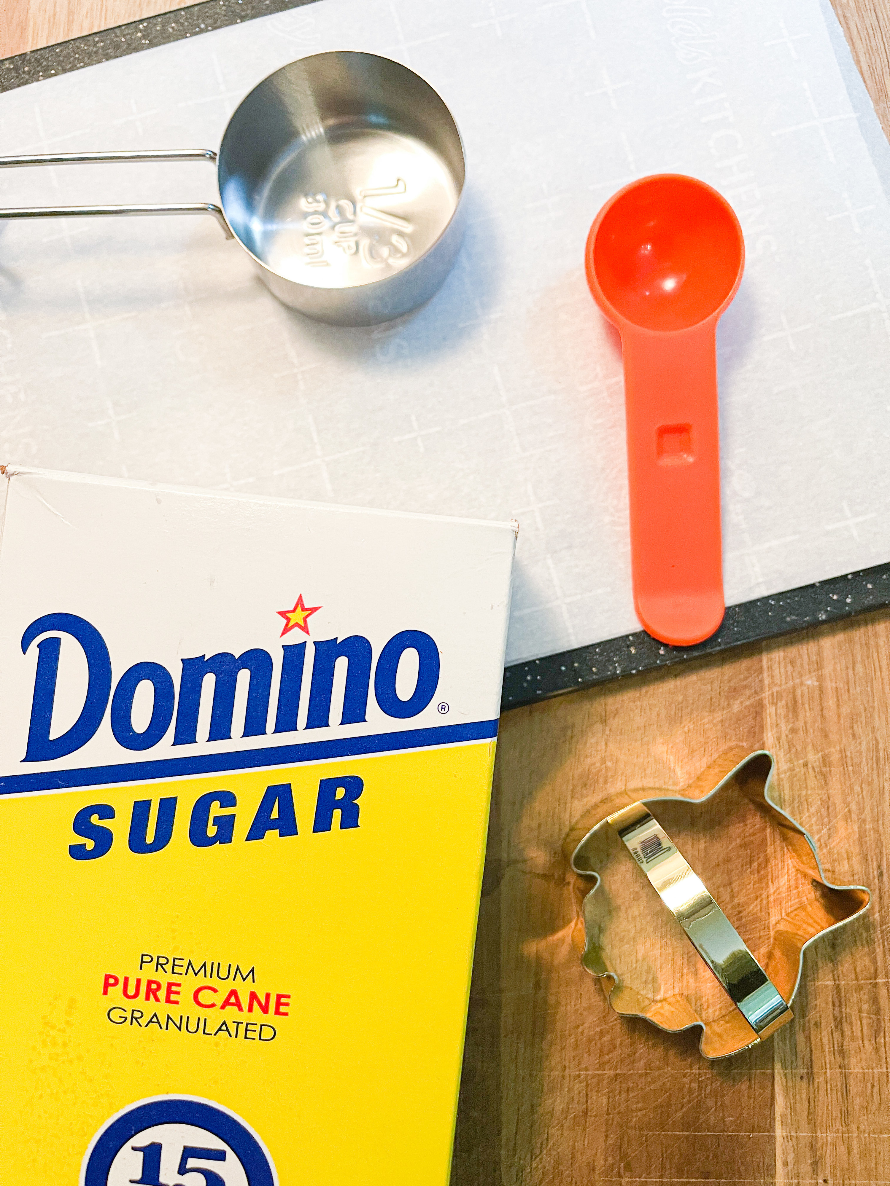 Cutting board with parchment paper, measuring cup, measuring spoon, cookie cutter, and granulated sugar