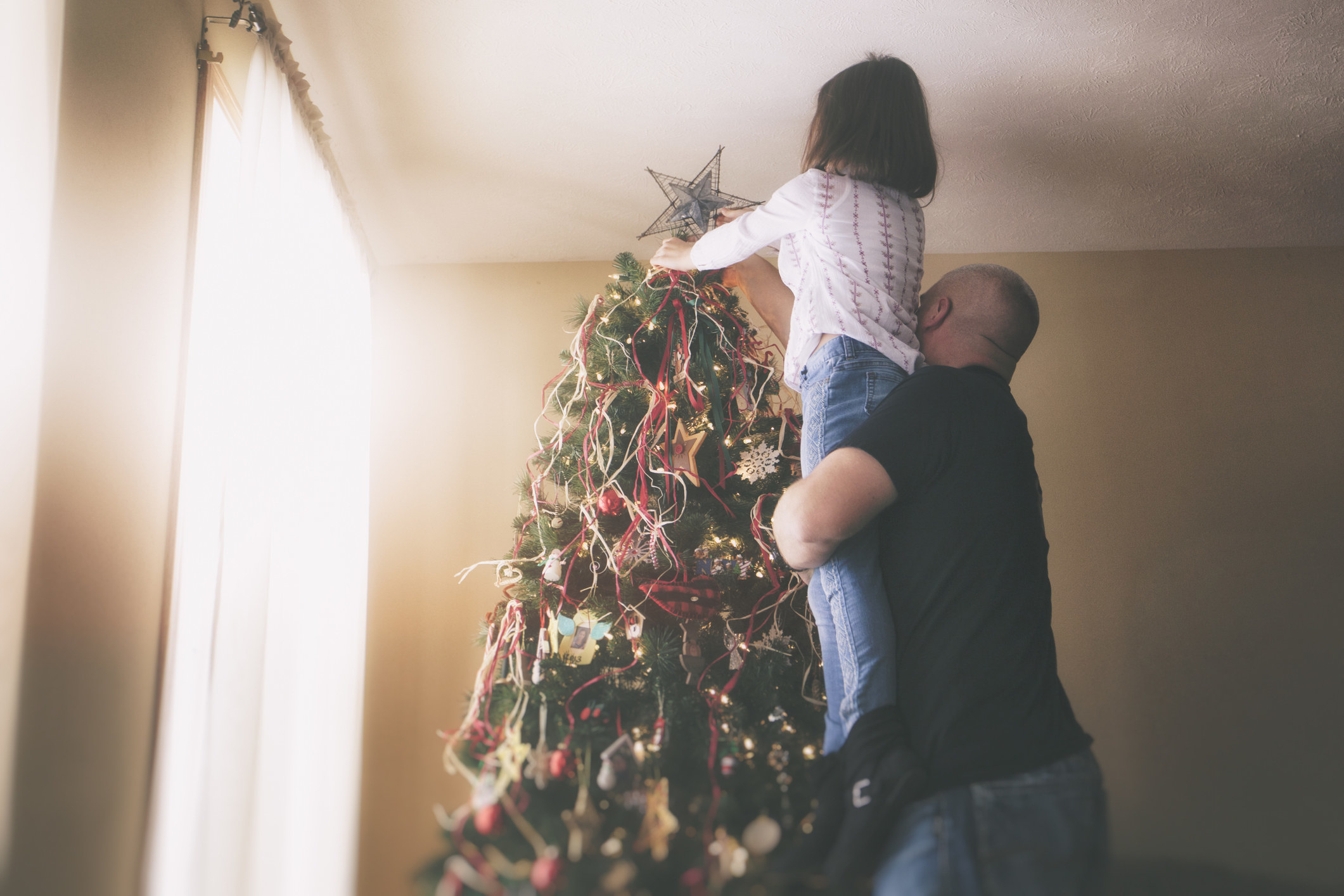 Man lifting his daughter up to put the star on top of the Christmas tree