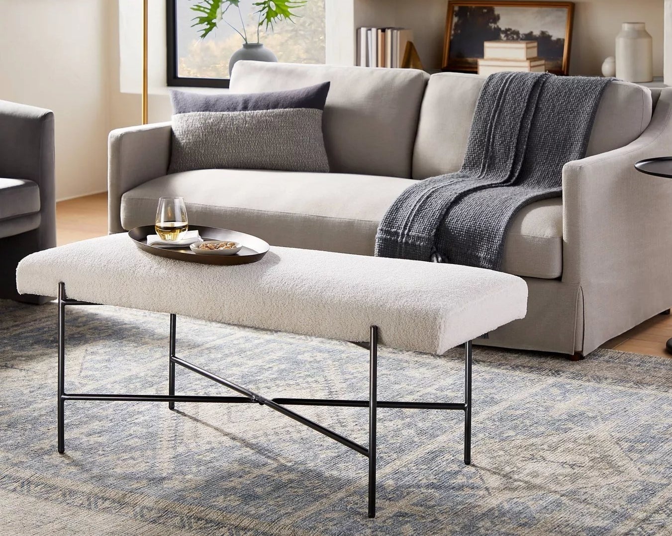 The boucle bench with black legs acting as a table in a living room