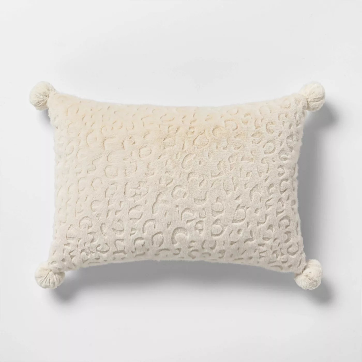 The ivory pillow with textured leopard spots and poms on every corner