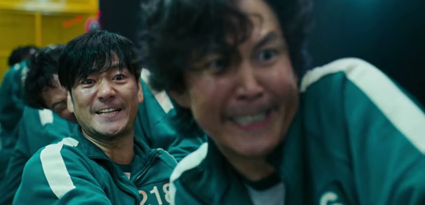 Gi-hun and Sang-woo look pained as they play tug of war