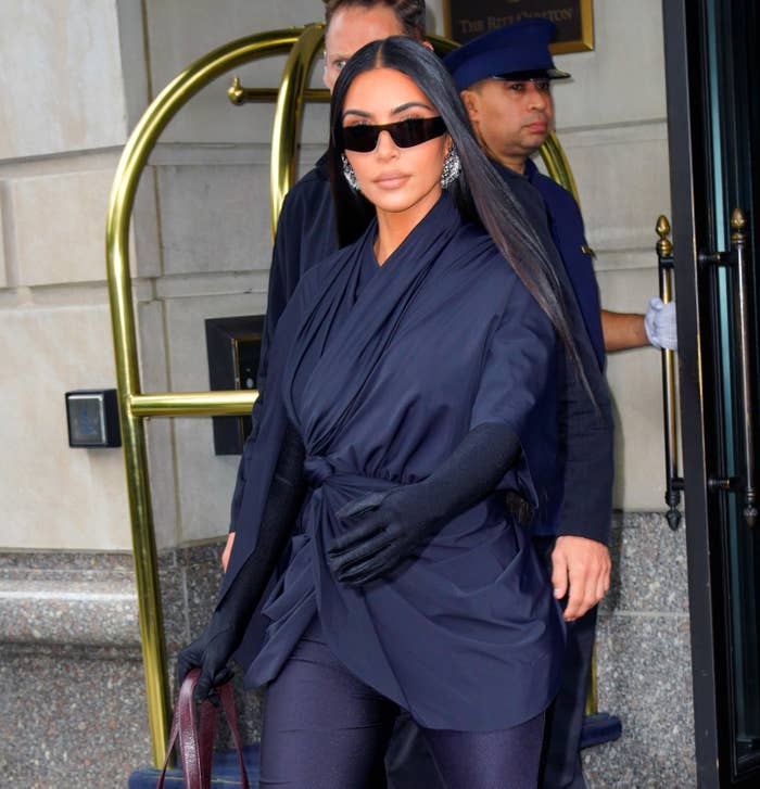 Kim walking out of a hotel in a head-to-toe dark ensemble and sunglasses