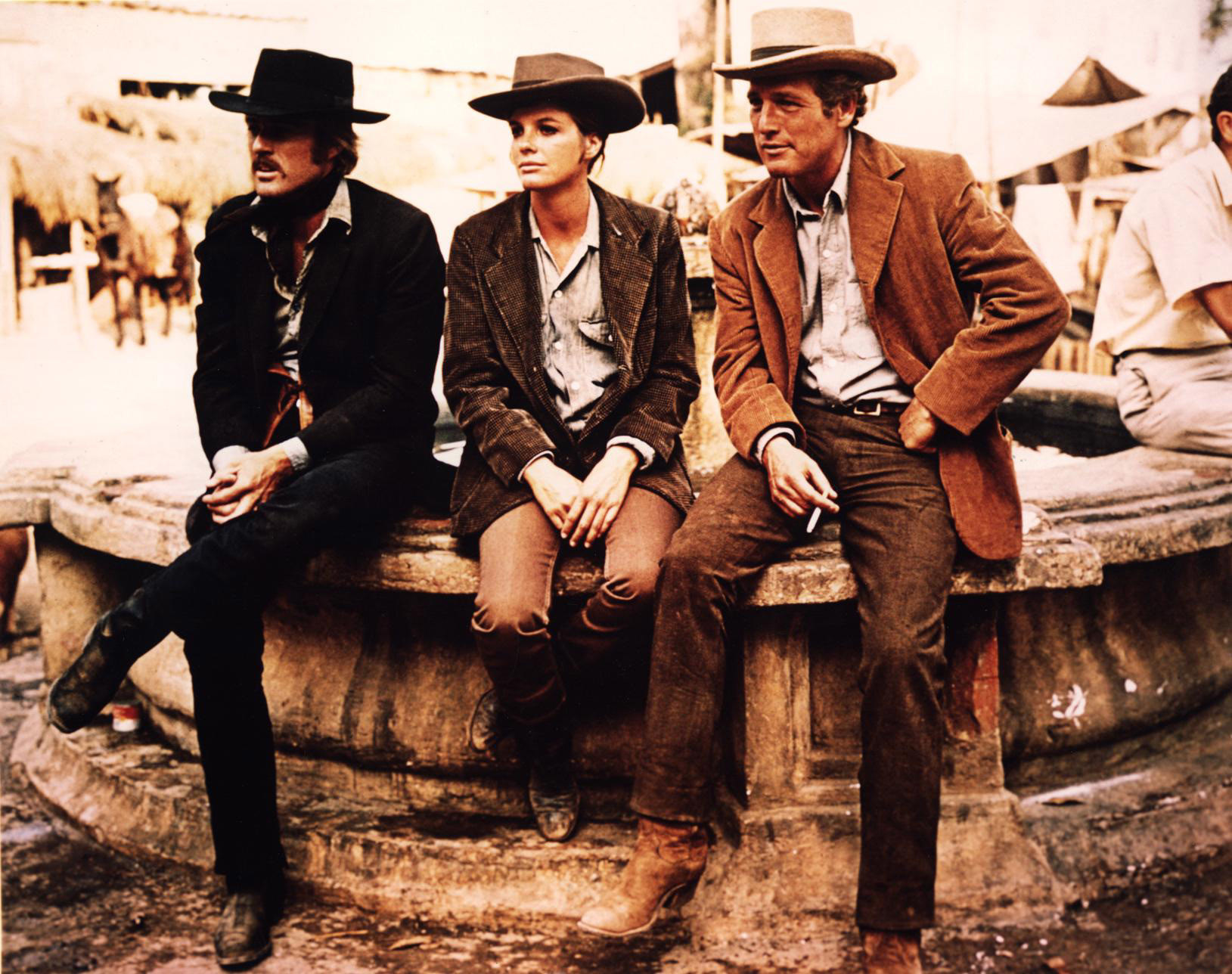 Robert Redford, Katharine Ross, and Paul Newman sit on a fountain in cowboy apparel