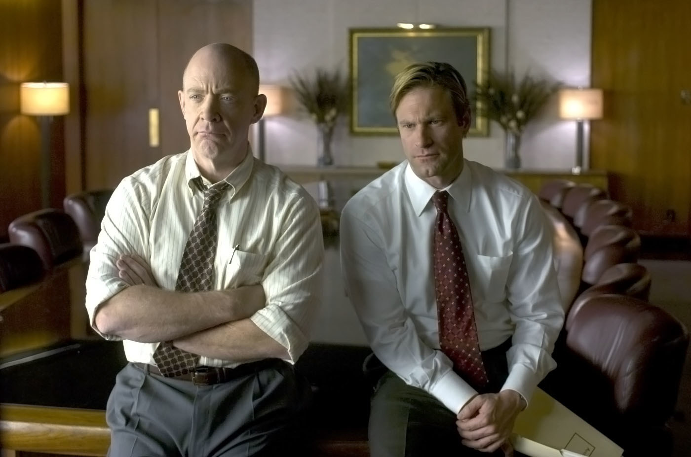 JK Simmons and Aaron Eckhart sit on a boardroom table