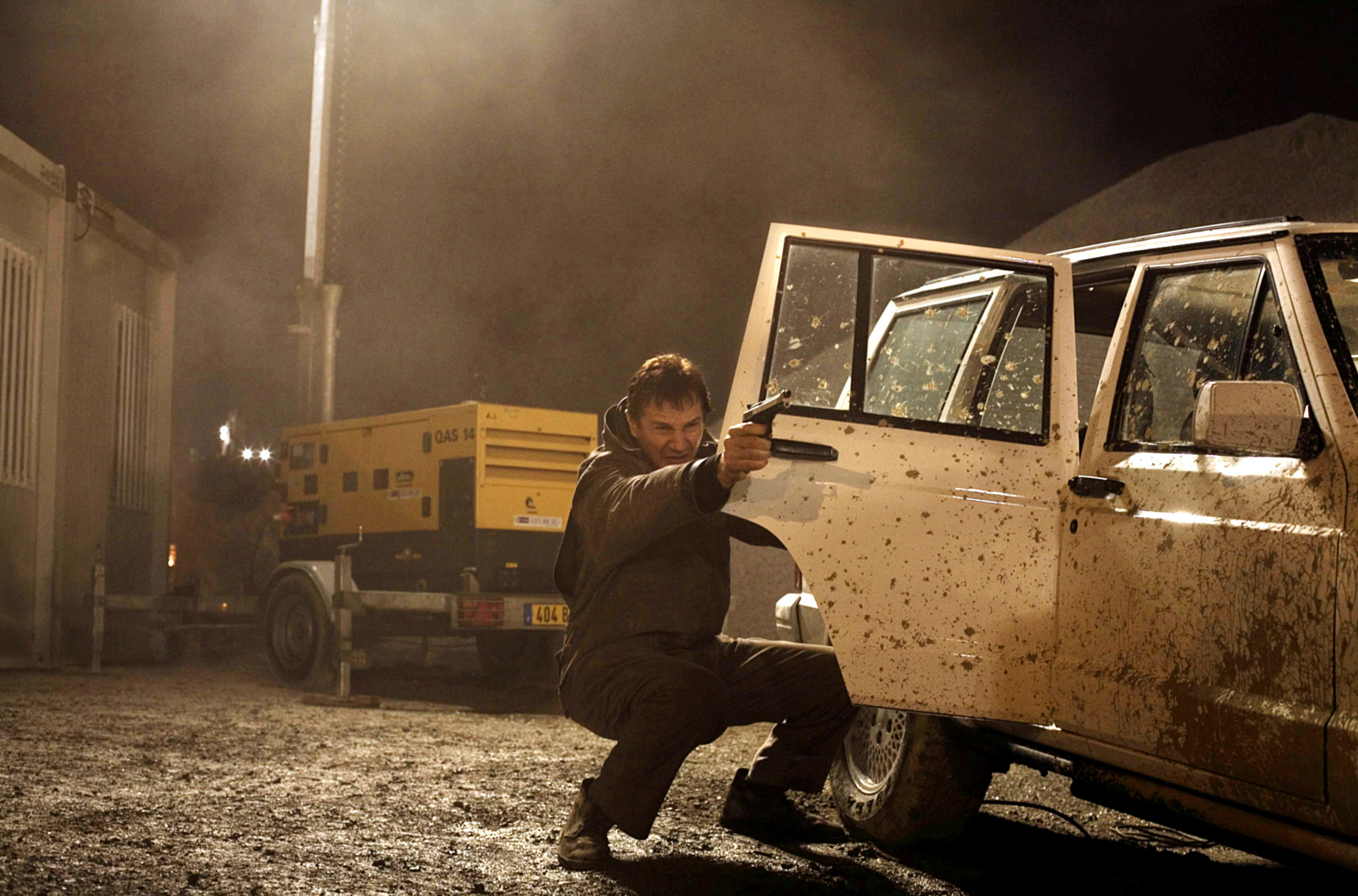 Liam Neeson shoots a gun from behind a car door