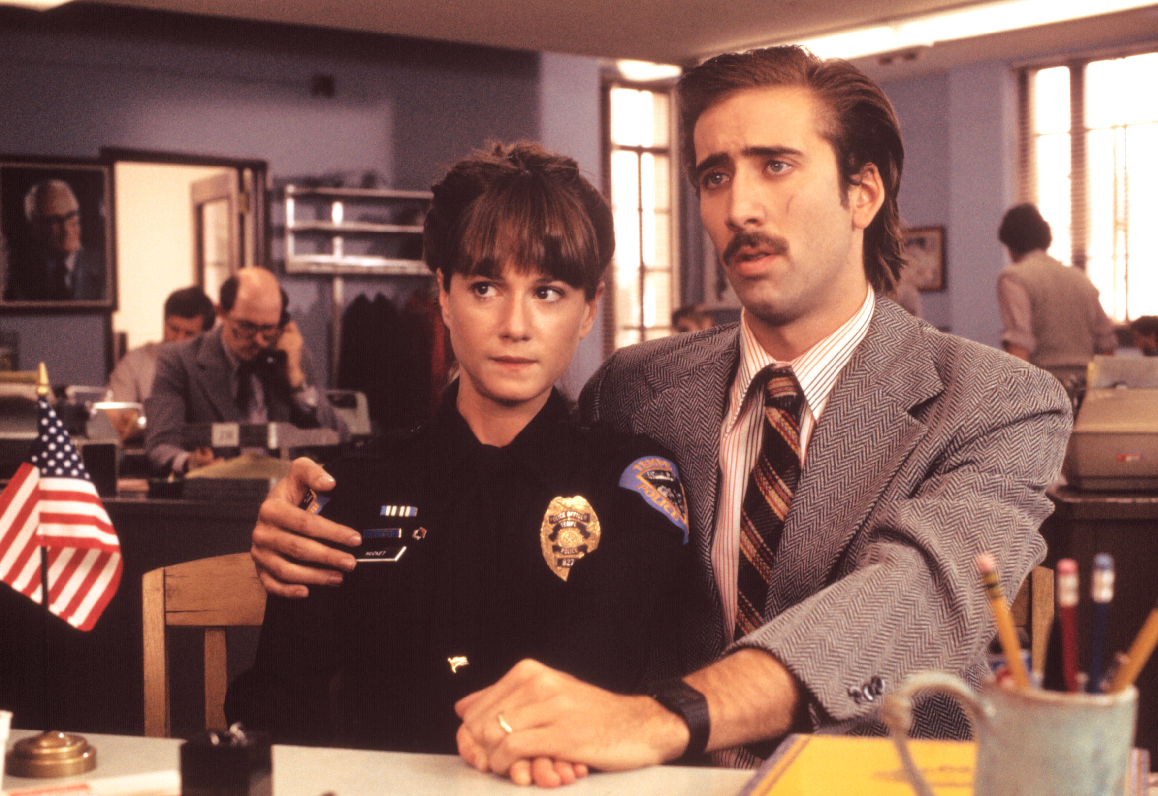 Holly Hunter, dressed in a police uniform, sits beside Nicolas Cage
