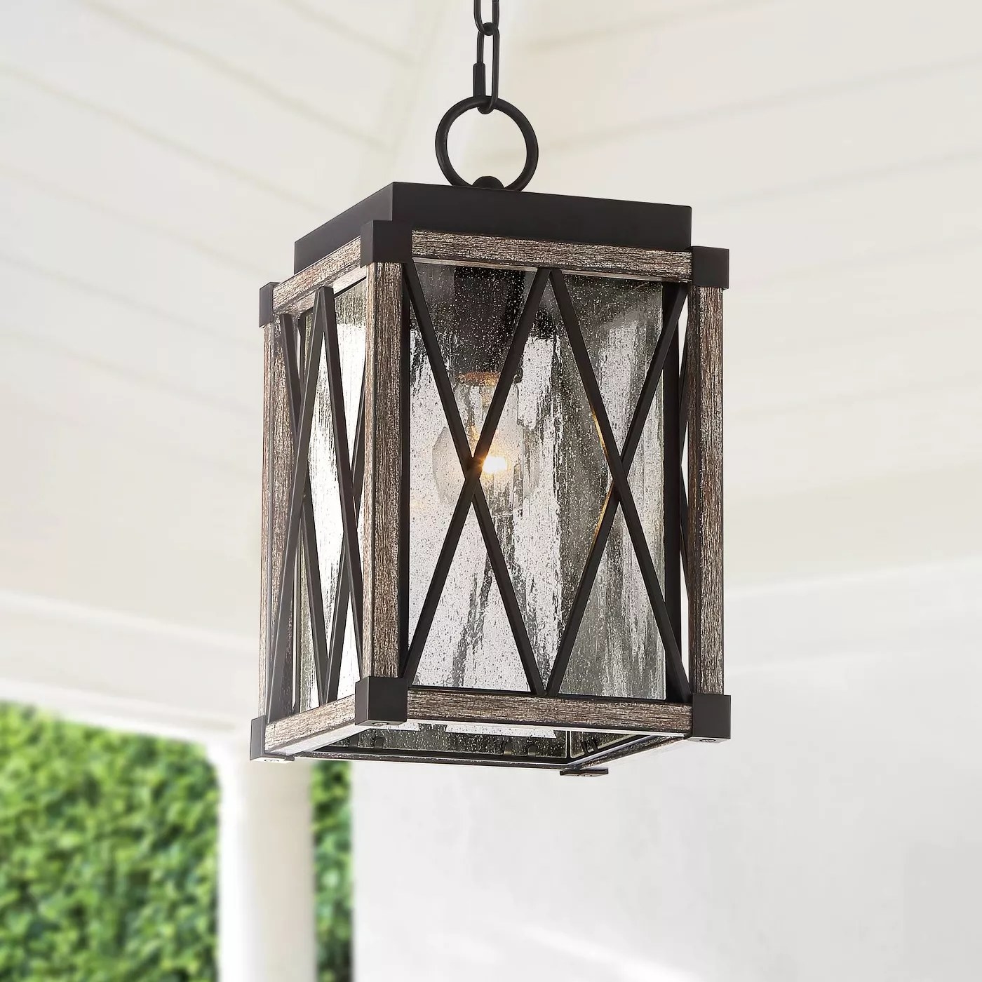 The lantern pendant with a wood and black frame and a single lightbulb hanging on a porch