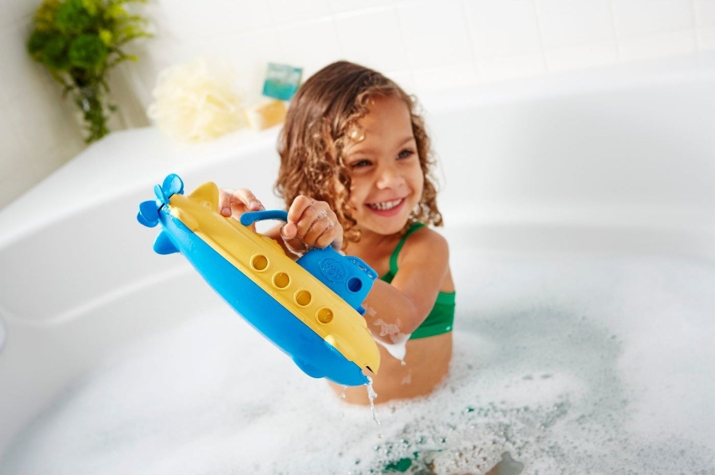 child in tub playing with yellow submarine