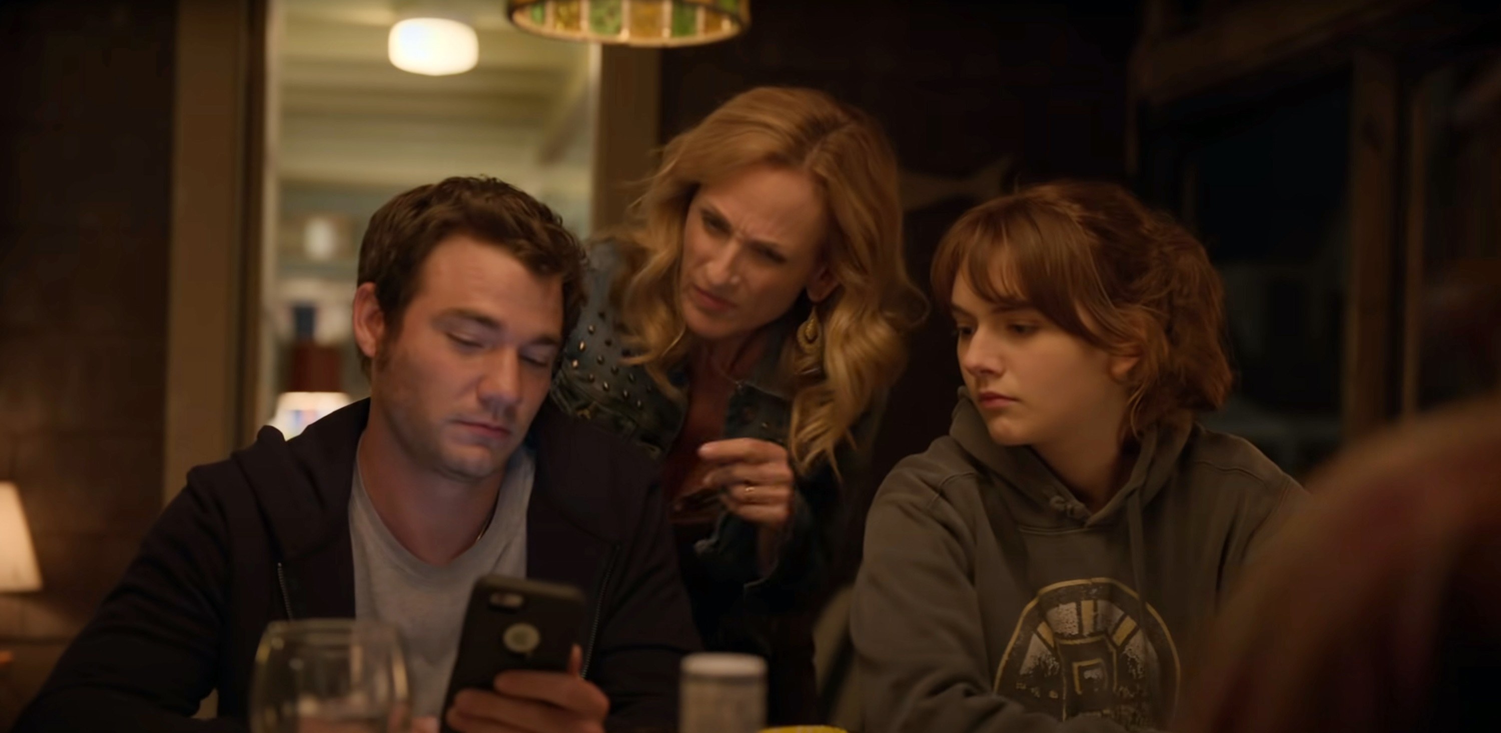 Daniel Durant, Marlee Matlin, and Emilia Jones look together at a phone at the dinner table