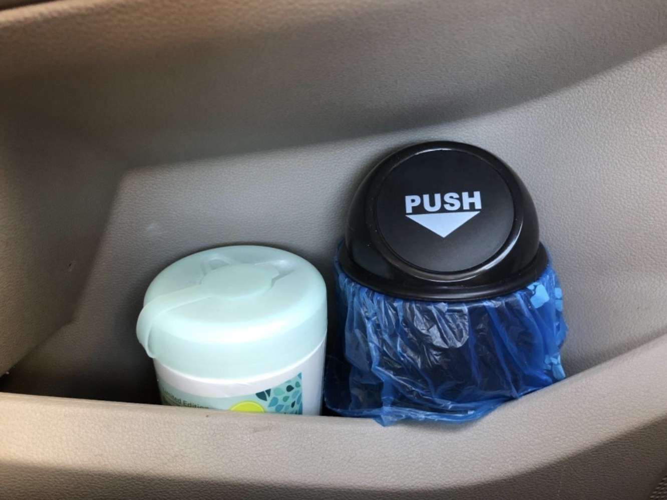 Tiny garbage can in car next to wipes on door