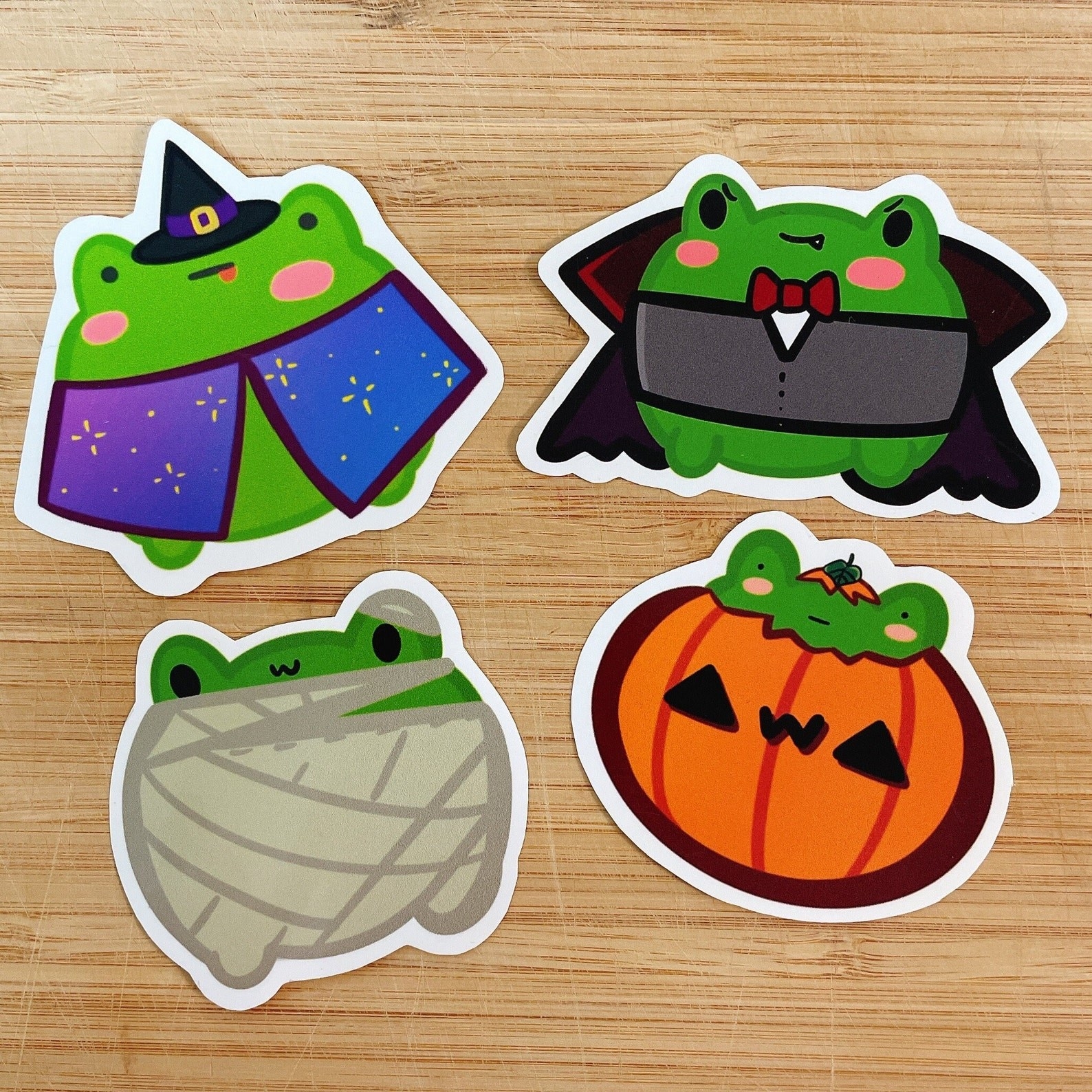 Four frogs dressed in a wizard costume, vampire costume, mummy costume, and pumpkin costume.