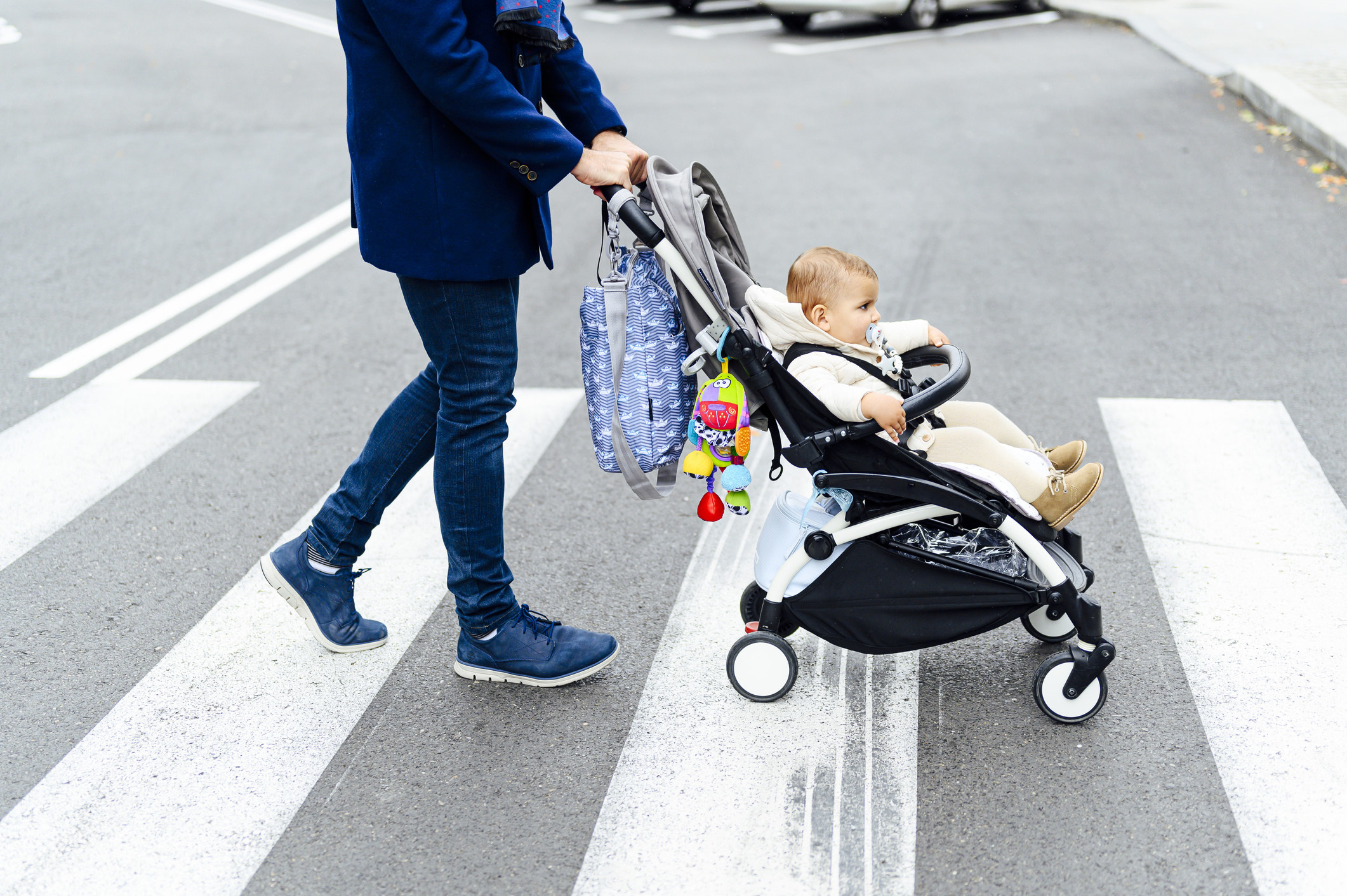A man walking a baby in a pram across a street