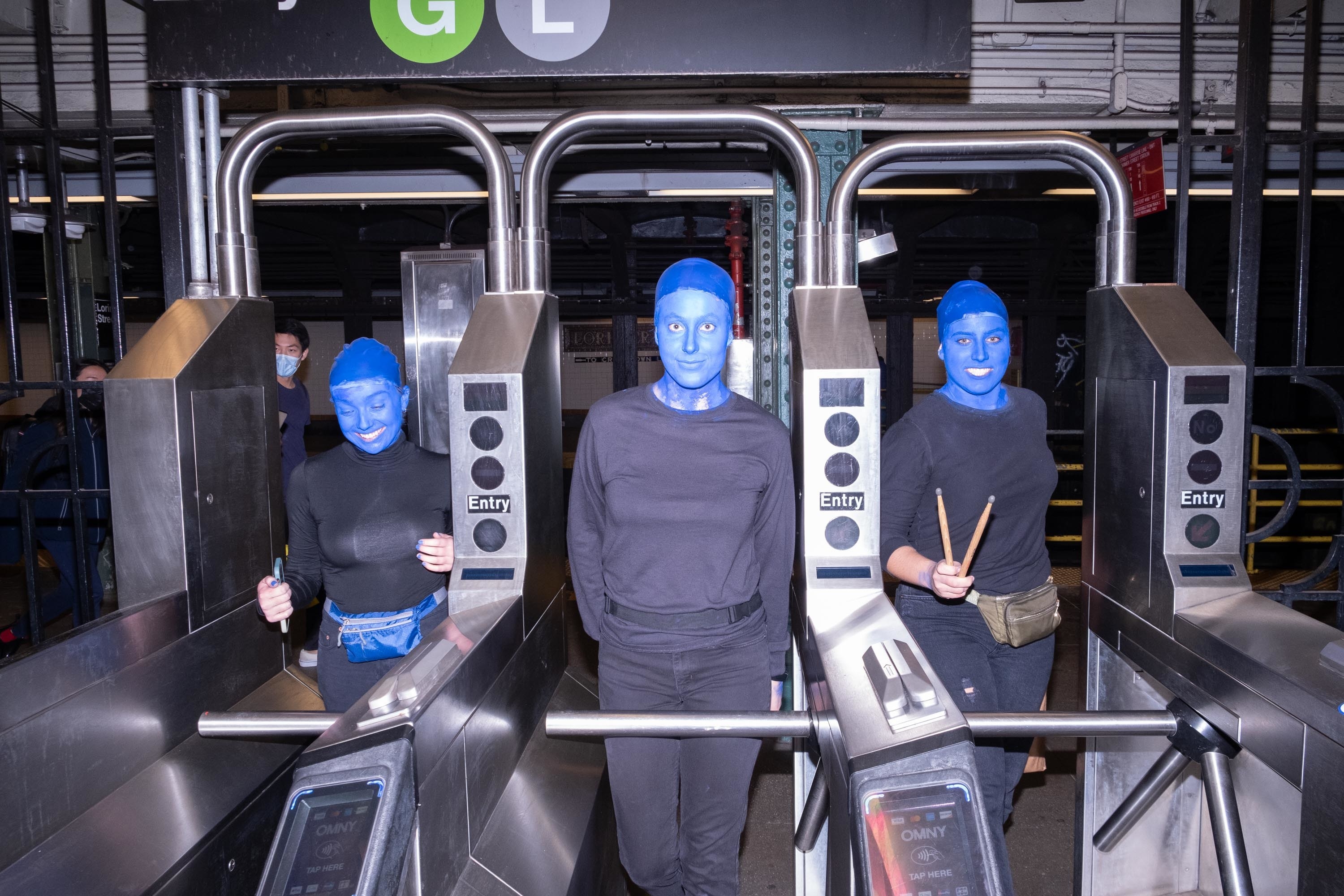 Three women dressed as blue men entering the subway through the turnstiles