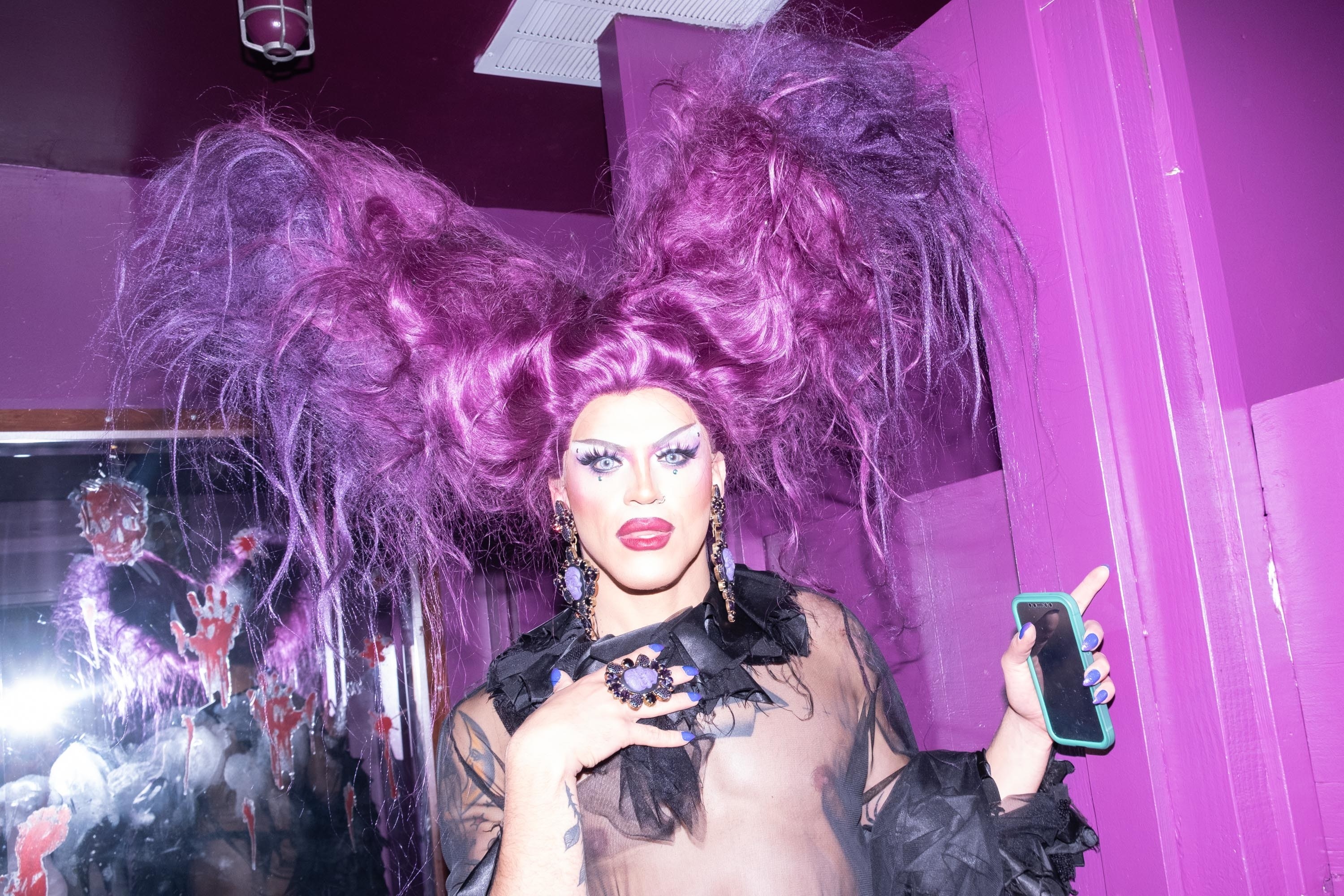 A drag queen with a massive purple wig in a purple bathroom 