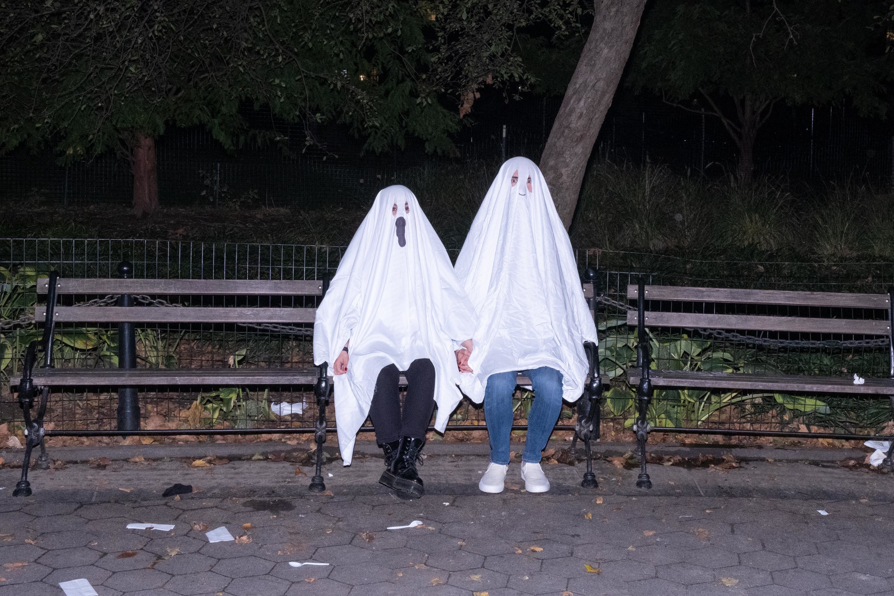Two people on a bench with sheets over their heads, dressed like ghosts