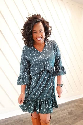 A reviewer wearing the three quarter-sleeve dress in teal with white polka dots with brown tall boots