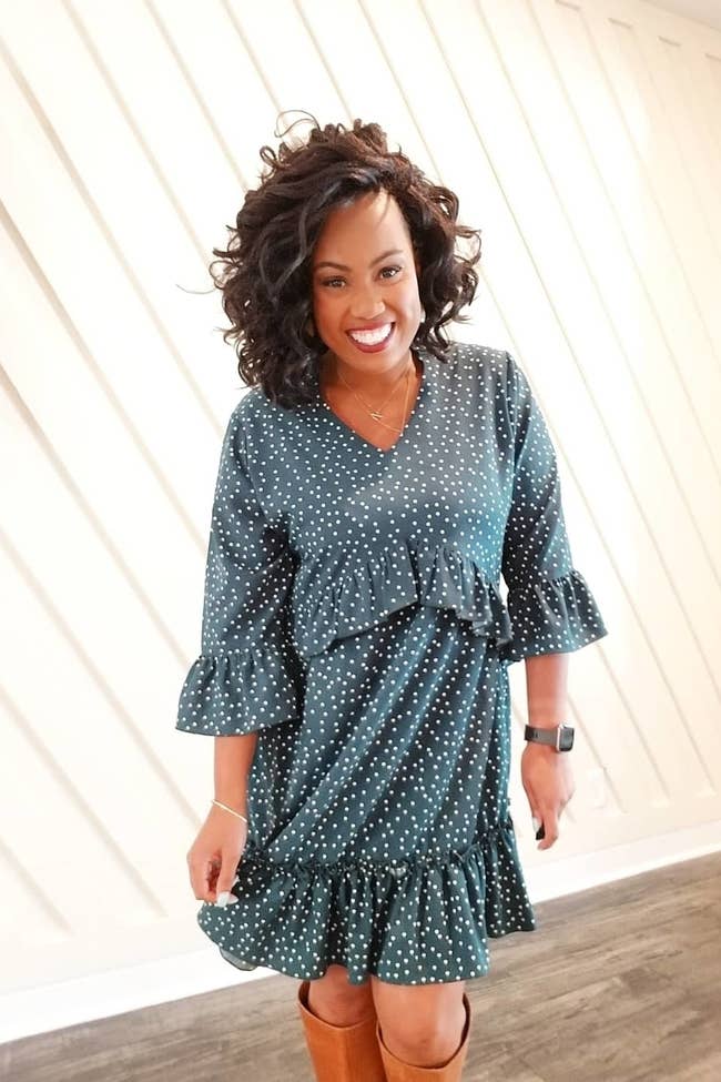 A reviewer wearing the three quarter-sleeve dress in teal with white polka dots with brown tall boots
