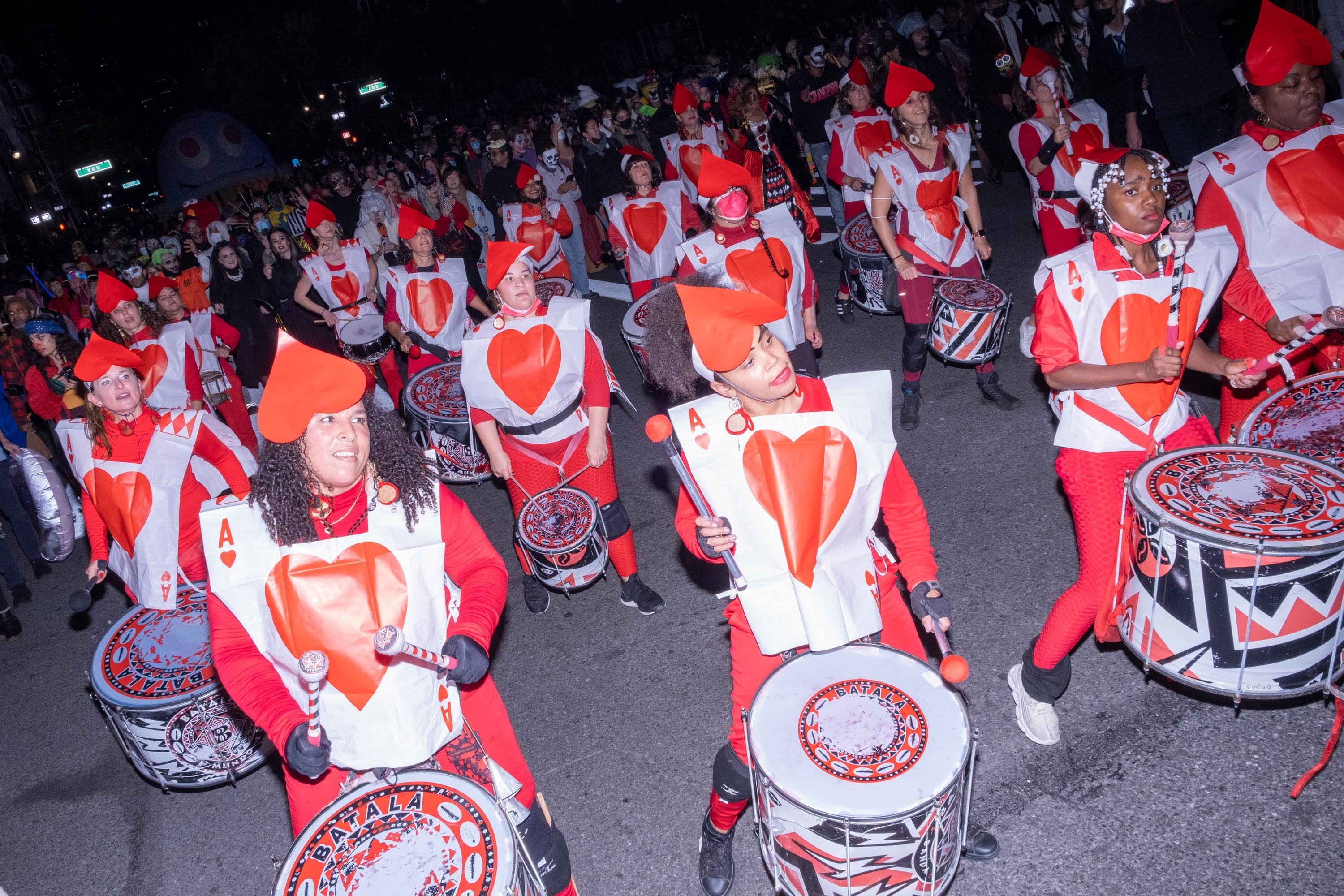 A large group of people dressed as playing cards banging drums