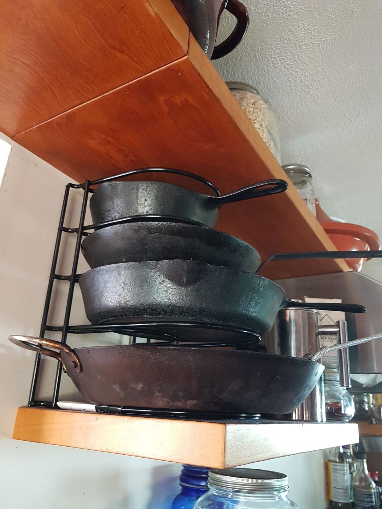 reviewer image of the black pan organizer with four cast iron pots on it