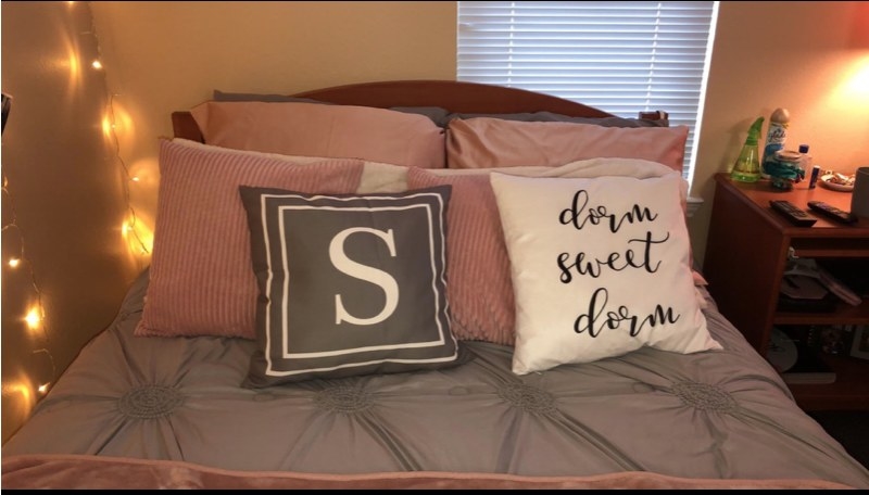 A white dorm sweet dorm pillow on a  reviewer&#x27;s pink and grey bed
