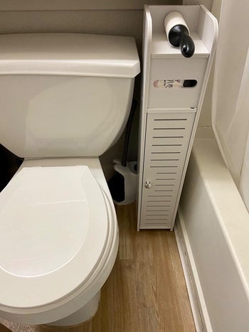 Reviewer photo showing how the toilet paper holder can fit into a narrow space between their toilet and bathtub