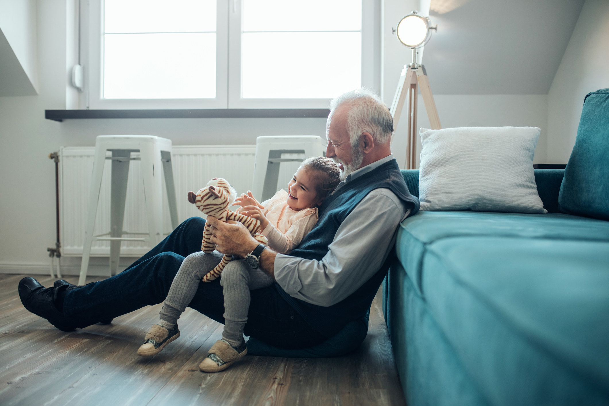 A grandfather holding his granddaughter while they play with a stuffed toy