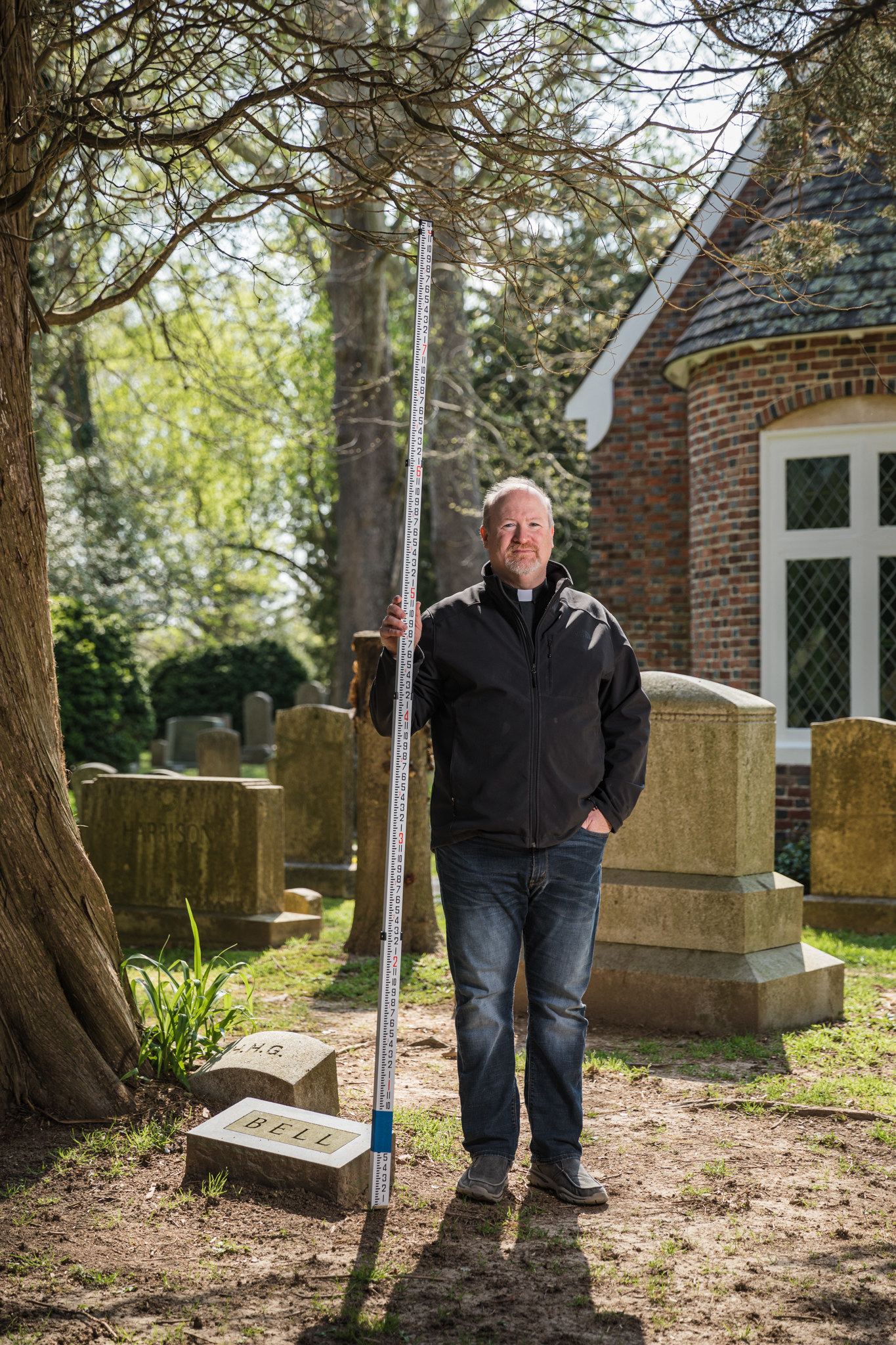 A priest holds a depth marker in front of a gravesite.