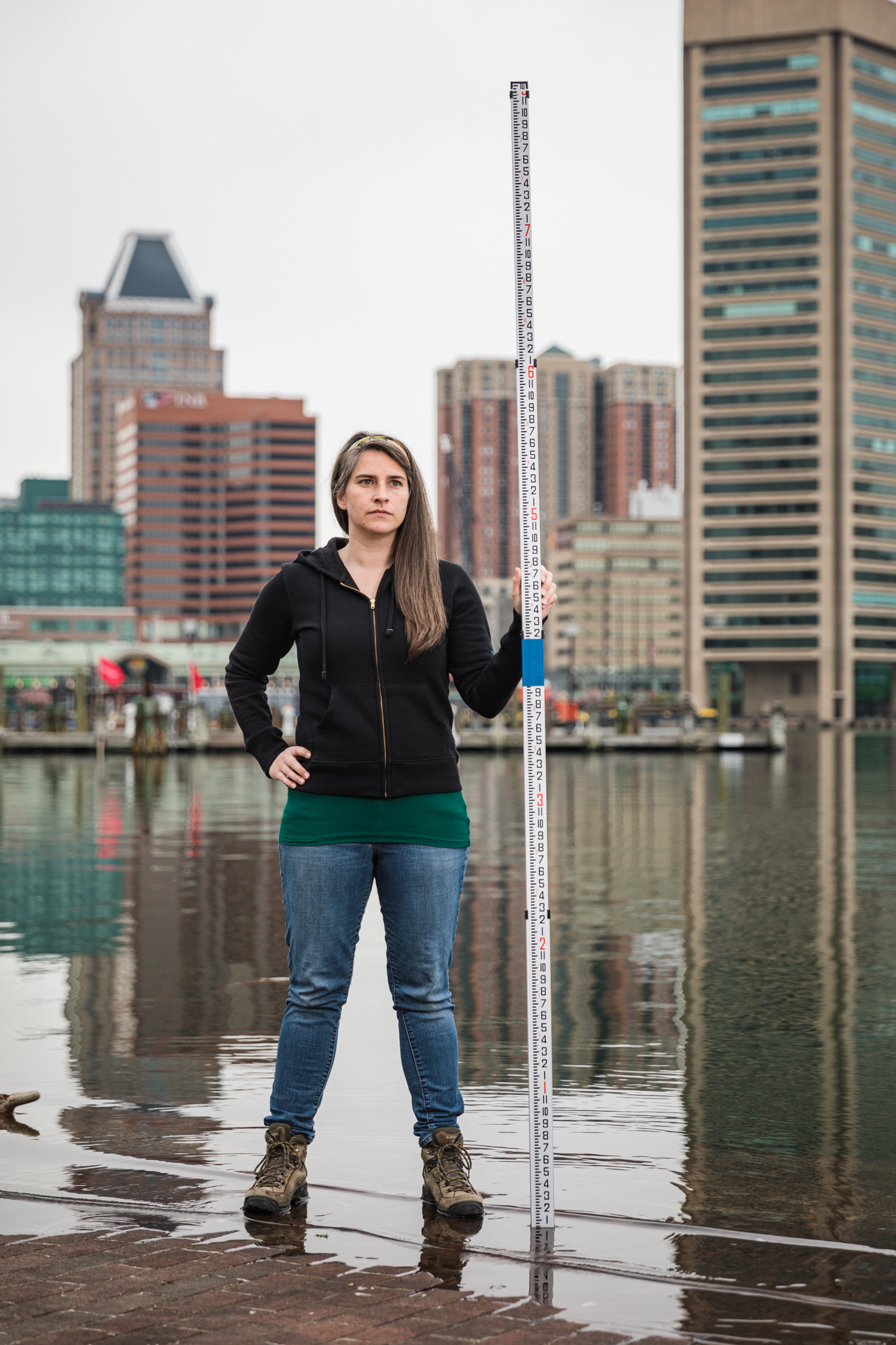 A woman stands in front of the Baltimore skyline, the water lapping at her feet.