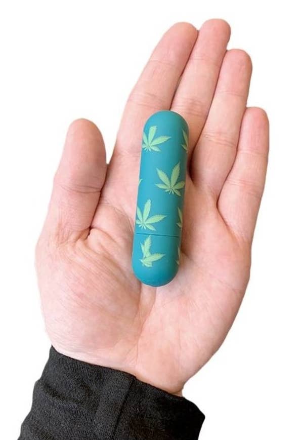 Model holding teal and green bullet vibrator with marijuana leaf pattern