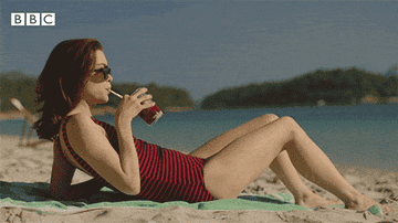woman laying on the beach drinking a red drink