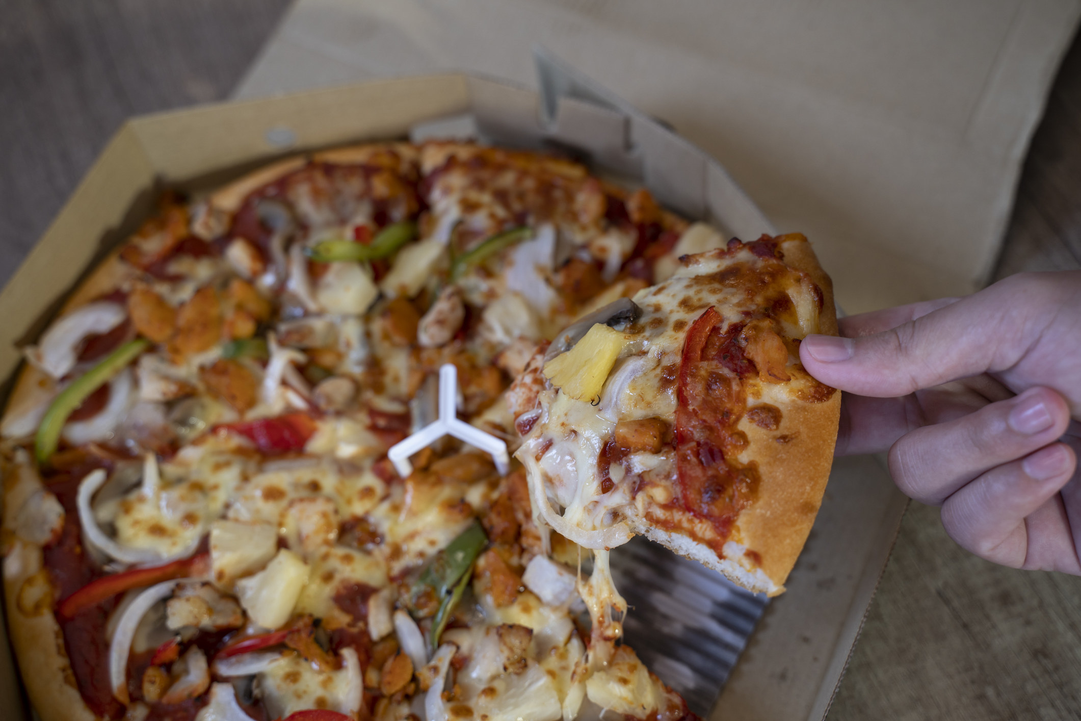 A hand taking a piece of pizza from a pie.