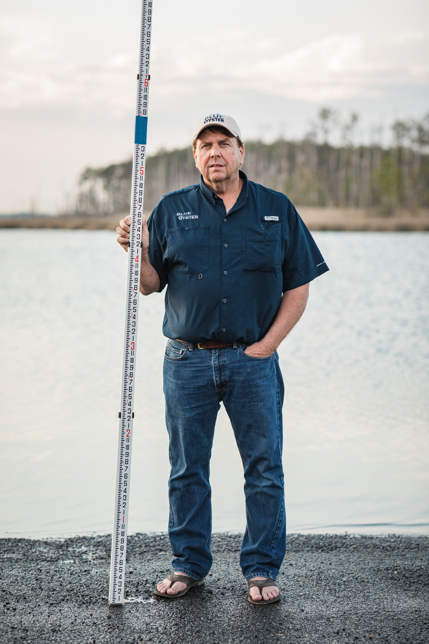 A man wearing flip flops stands outside holding a depth marker