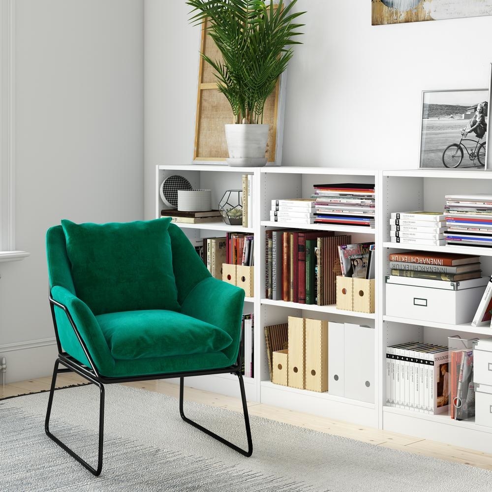green velvet accent chair next to white bookshelf packed with books and journals