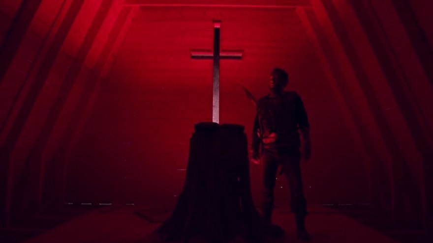 Nicolas Cage stands in a bright red room next to a cross set on a pedestal