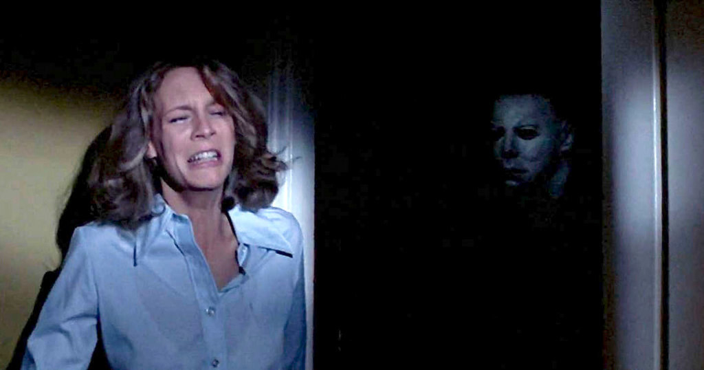 Laurie is resting by the dark doorway and Michael Myers&#x27; mask slowly comes into view