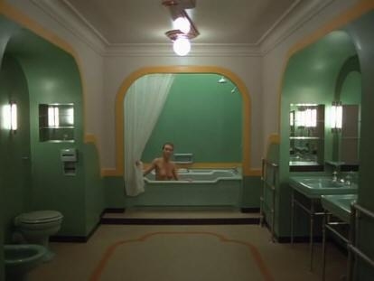A hideous green bathroom with the bathtub in the center; the shower curtain begins to eerily move and shows a naked young woman sitting in the tub