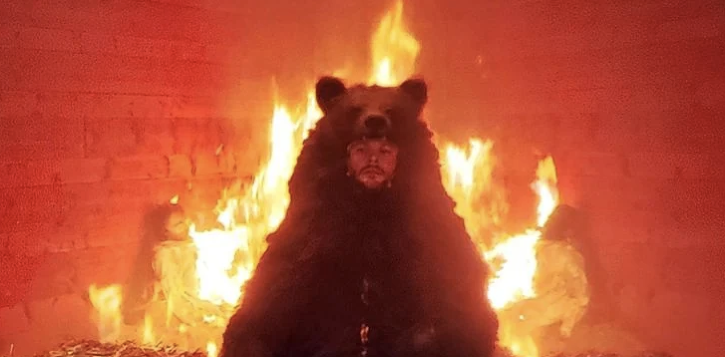 Christian sits paralyzed dressed in a bear costume as the temple around him goes up in flames; there are also other burning victims in the background