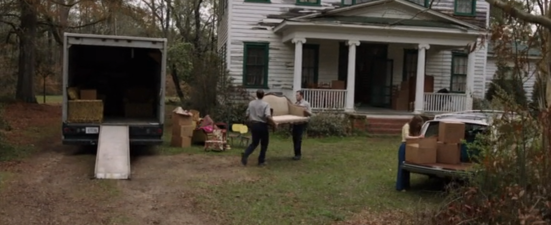 A moving truck sits beside a house as the family moves in their stuff; two men carry in a couch