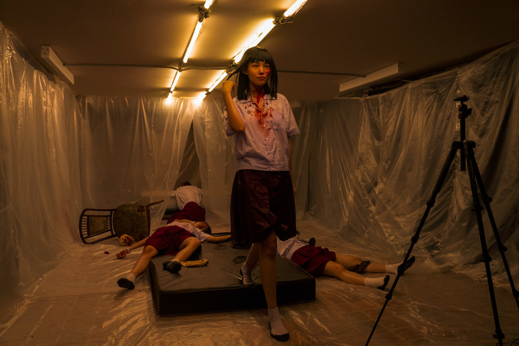 A final girl standing with blood on her face in a creepy, plastic covered room