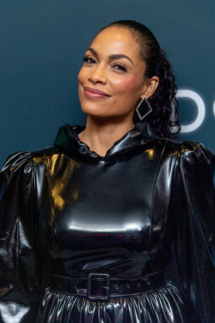 Rosario Dawson smiles with her head tilted at a red carpet event